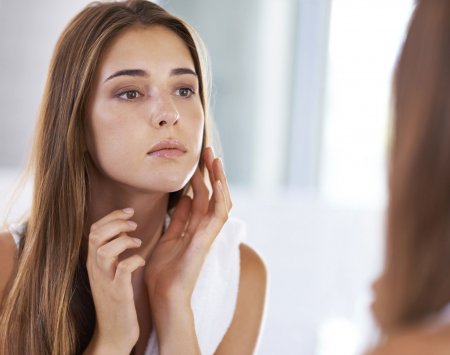 Une femme regarde sa peau dans un mirroir