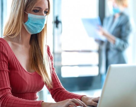 Femme derrière un ordinateur avec un masque